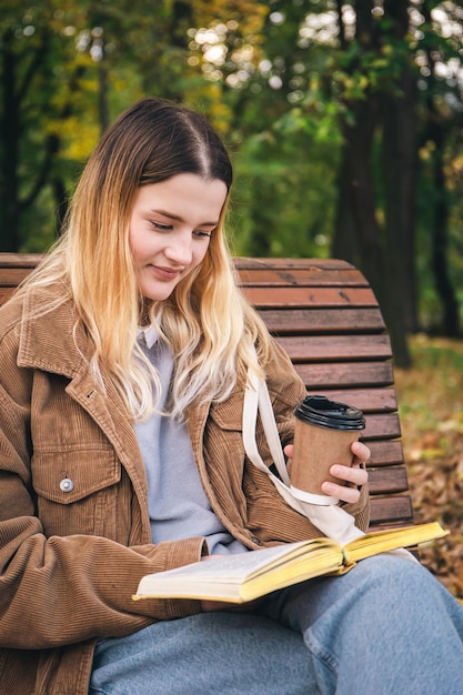 Een aantrekkelijke jonge vrouw zit op een bankje in een herfstpark en leest een boek