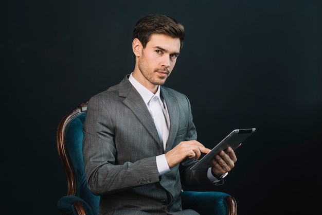 Een aantrekkelijke jonge zakenmanzitting in leunstoel die digitale tablet gebruiken