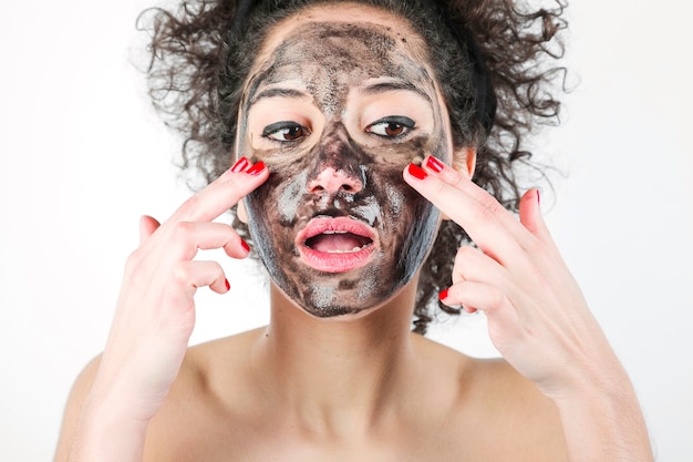 Een aantrekkelijke vrouw die zwart gezichtsmasker met haar vingers toepast tegen witte achtergrond