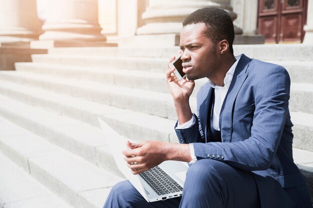 Een Afrikaanse jonge mensenzitting op laptop die van de trapholding op mobiel spreken