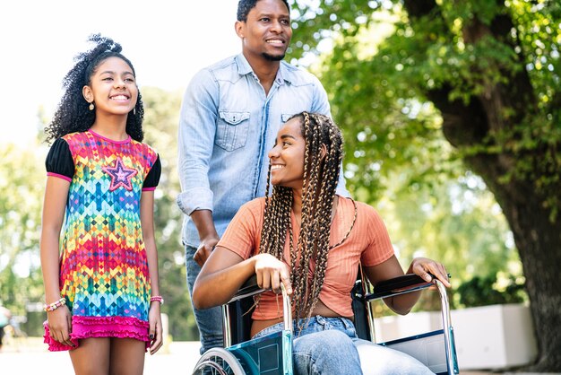 Een Afro-Amerikaanse vrouw in een rolstoel die geniet van een wandeling buiten met haar dochter en echtgenoot.