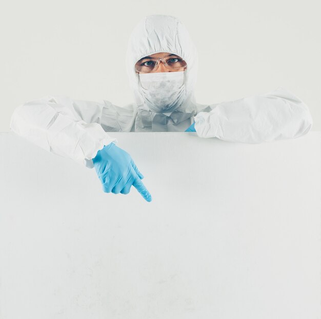 Een arts in masker, handschoenen en beschermende pak naar beneden wijst in wit oppervlak