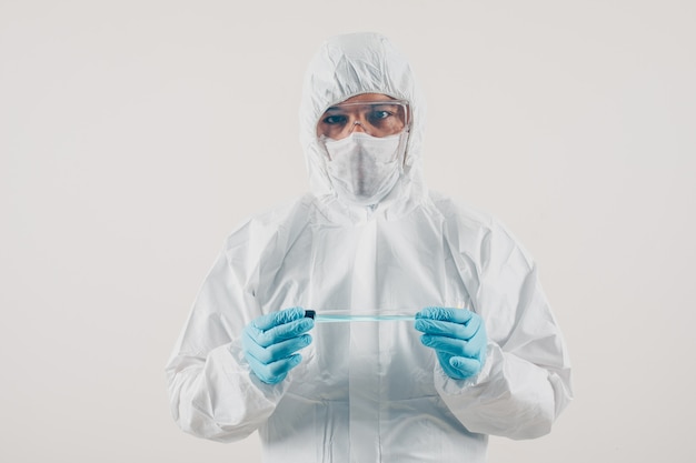 Een arts in medische handschoenen en beschermend kostuum die en geneeskunde op lichte achtergrond bevinden zich houden. coronavirus
