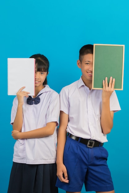 Een Aziatische student die een notitieboekje houdt en Aziatische mannelijke student die een groen raad op een blauw houdt.