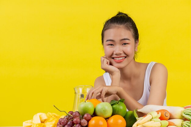 Een Aziatische vrouw die een wit mouwloos onderhemd draagt. De tafel staat vol met vele soorten fruit.