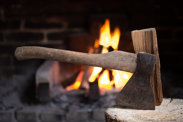 Een bijl die vastzit in een houten stronk bij een brandende open haard. Het concept van comfort en ontspanning in het dorp.