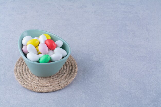 Een blauwe diepe kom vol kleurrijke bonen snoepjes op grijze tafel.