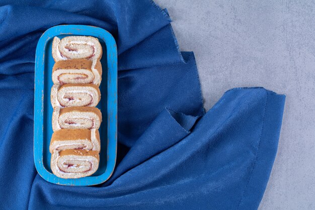Een blauwe houten plank met zoete gesneden broodjes op tafelkleed.