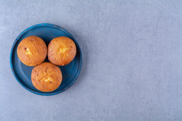 Een blauwe houten plank van drie zoete verse cupcakes.