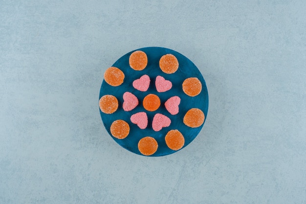 Een blauwe houten plank vol oranje suikerachtige gelei-snoepjes met hartvormige gelei-snoepjes