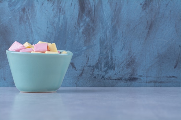 Een blauwe kom vol roze en gele zoete zoetwaren Pastila.