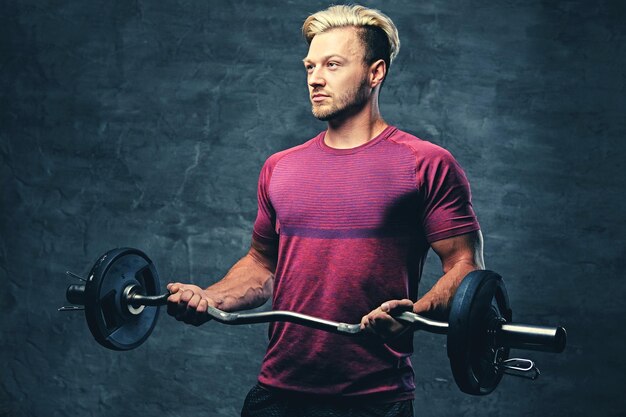 Een blonde, atletische man gekleed in een rode sportkleding houdt barbeel vast.