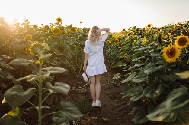 Een blonde vrouw in een witte jurk op het veld met zonnebloemen