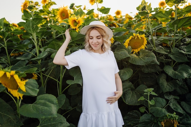 Een blonde vrouw in een witte jurk op het veld met zonnebloemen