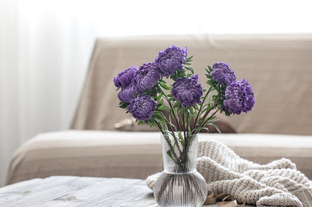 Een boeket blauwe chrysanten in een glazen vaas op de tafel in het interieur van de kamer.