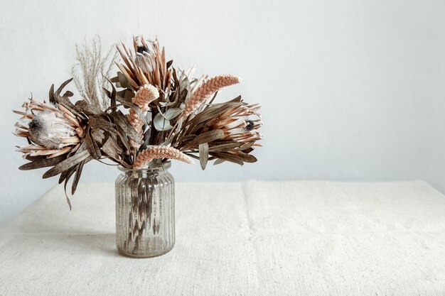 Een boeket gedroogde bloemen in een glazen vaas op een lichte achtergrond