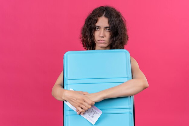 Een boos vrouw met kort haar, gekleed in een groene crop top met blauwe koffer en vliegtickets