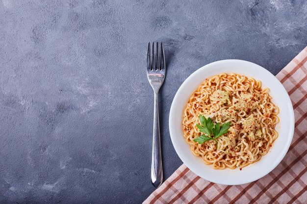 Een bord pasta in het midden op blauwe tafel.