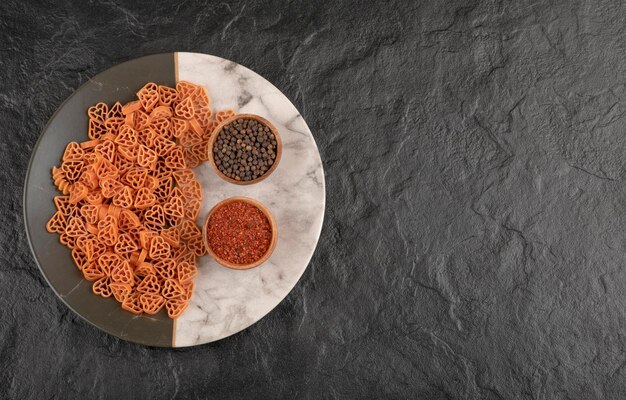 Een bord rauwe pasta in hartvorm met peper op zwarte tafel