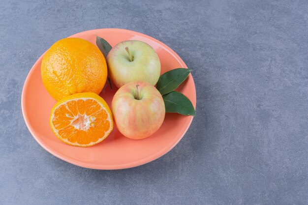 Een bord smakelijke appel en sinaasappels op het donkere oppervlak