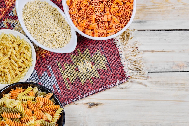 Een bos van kleurrijke ongekookte pastakommen op houten lijst met gesneden doek.