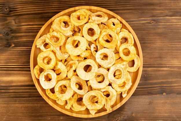 Een bovenaanzicht ananas gedroogde ringen in plaat gedroogd fruit zure smakelijke unieke smaak op het bruine houten bureau fruit exotische droge