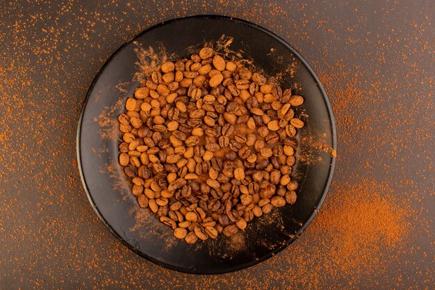 Een bovenaanzicht bruine koffie zaden in zwarte plaat op de bruine tafel