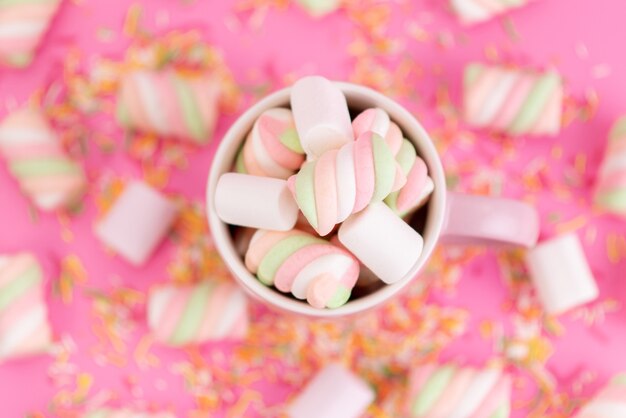 Een bovenaanzicht die marshmallows kauwt in een roze beker en alles op een roze bureau