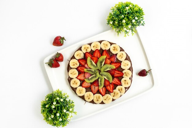 Een bovenaanzicht fruit choco cake ontworpen met verse gesneden bananen, aardbeien en kiwi's in witte plaat suiker zoet dessert