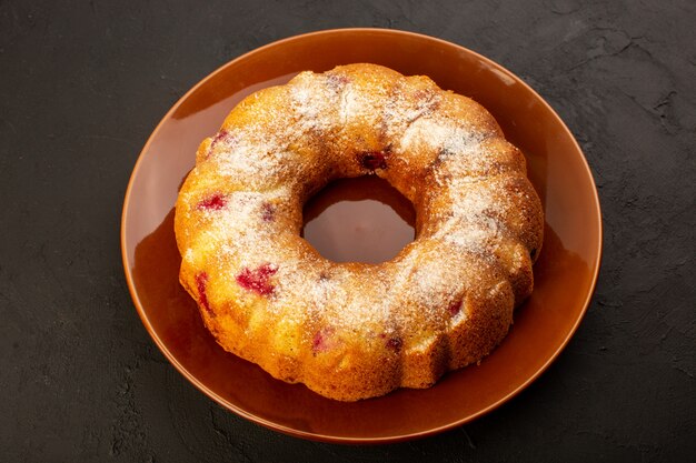 Een bovenaanzicht gebakken fruitcake heerlijke ronde met rode kersen binnen en suikerpoeder binnen ronde bruine plaat op donker