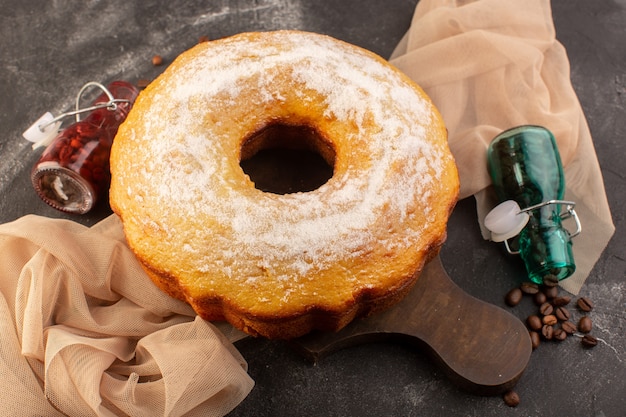 Een bovenaanzicht gebakken ronde cake met suikerpoeder en koffiezaden op het houten bureau