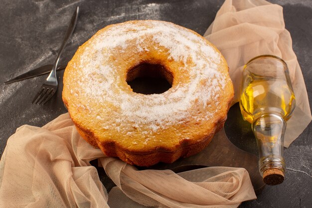 Een bovenaanzicht gebakken ronde cake met suikerpoeder en olijfolie op het houten bureau