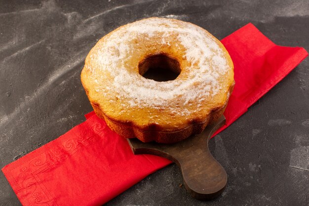 Een bovenaanzicht gebakken ronde cake met suikerpoeder op het houten bureau
