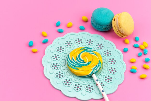 Een bovenaanzicht gekleurde lolly met Franse macarons en snoepjes op roze bureau, snoep kleur zoete suiker