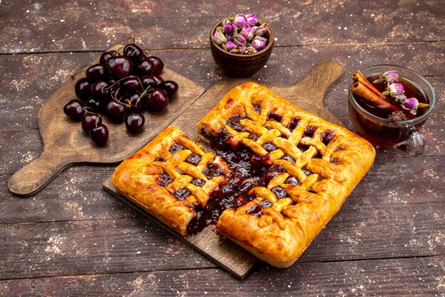 Een bovenaanzicht heerlijke aardbeientaart met aardbeigelei kersen en thee op de houten achtergrond cake koekje suiker