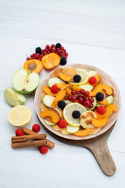 Een bovenaanzicht in de verte vers gesneden fruit kleurrijk en rijp op het houten bureau en witte achtergrond fruit kleur voedsel foto