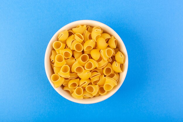 Een bovenaanzicht italia droge pasta vormde kleine gele rauwe pasta in crèmekleurige ronde kom geïsoleerd op de blauwe achtergrond Italiaanse spaghetti food pasta
