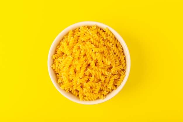 Een bovenaanzicht italia droge pasta vormde kleine gele rauwe pasta in crèmekleurige ronde kom geïsoleerd op de gele achtergrond Italiaanse spaghetti food pasta