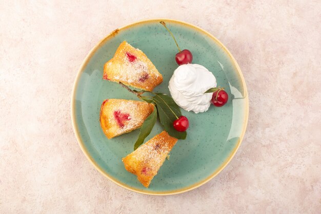 Een bovenaanzicht kersencake plakjes lekker binnen ronde plaat op het roze bureau bisicuit cake suiker fruit