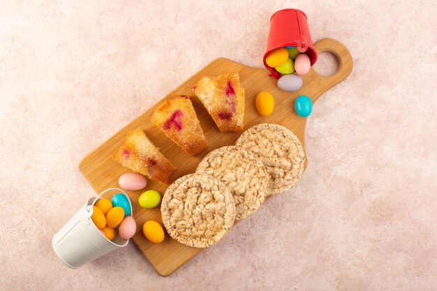 Een bovenaanzicht kersencake plakjes met snoepjes en koekjes op de helderroze desk cake koekjessuiker