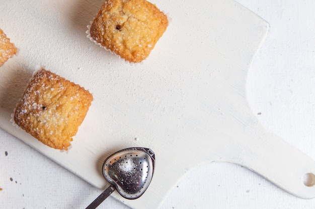 Een bovenaanzicht kleine cakes gebakken en lekker in papier formulieren met suiker poeder op het witte bureau