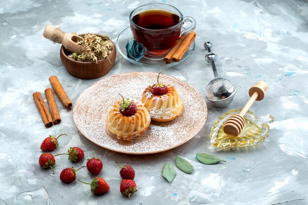 Een bovenaanzicht kleine lekkere cakes met rode aardbeien, kaneel en theecake fruit