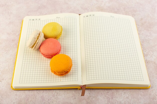 Een bovenaanzicht kleurde Franse macarons op het voorbeeldenboek en het roze zoete koekje van de bureaucake