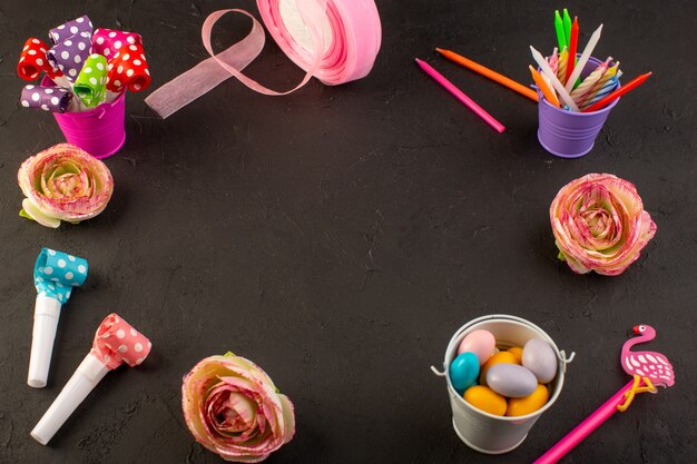 Een bovenaanzicht kleurrijke decoraties zoals snoeppotloden en bloemen op het donkere bureau verjaardag kleurdecoratie