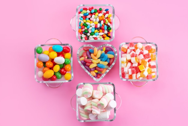 Een bovenaanzicht kleurrijke snoepjes en marshmallows in glazen op roze bureau, kleur zoete suiker