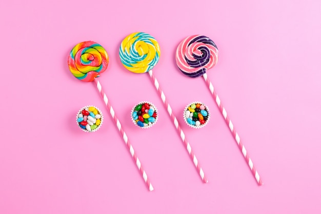Een bovenaanzicht kleurrijke zoete lollies op de roze-witte suikersticks en veelkleurige snoepjes op de roze achtergrond verjaardag regenboog