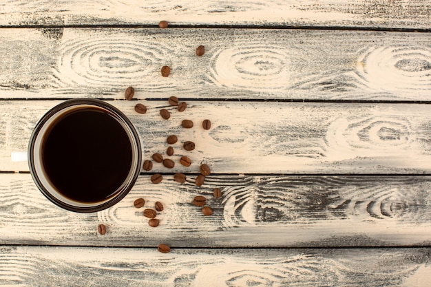 Een bovenaanzicht kopje koffie met bruine koffiezaden op het grijze rustieke bureau drinkt koffiekleur