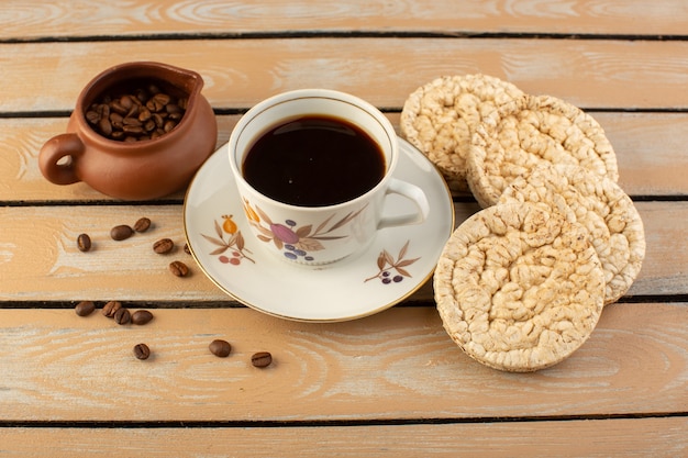 Een bovenaanzicht kopje koffie warm en sterk met verse bruine koffiezaden en crackers op de crème rustiek bureau koffiezaad drank foto graan