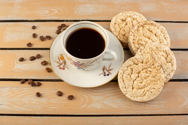 Een bovenaanzicht kopje koffie warm en sterk met verse bruine koffiezaden en crackers op de crème rustiek bureau koffiezaad drank foto graan