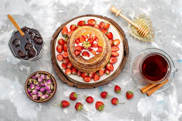 Een bovenaanzicht lekkere ronde pannenkoeken met cream tea en rode aardbeien op de houten bureautaart